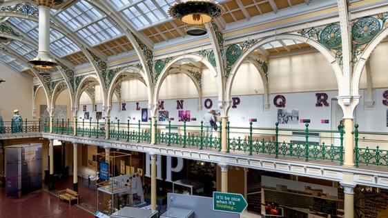 Side view of half of the Industrial Gallery balcony with ornate ironwork, gas lanterns hanging from a glazed ceiling.