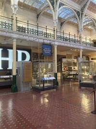 An exhibition area with lots of glazed cases on display and a large HP sign in the background, with ornate balcony above.