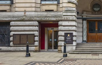 Historic stone building with with lift entrance and checkered pavement.