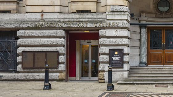 Historic stone building with with lift entrance and checkered pavement.