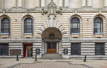 Historic stone building with arched windows, grand entrance, decorative sculptures, and checkered pavement.
