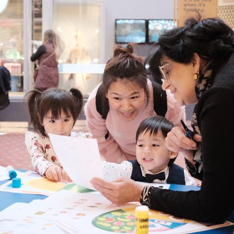 Adults and children looking at paper resource while doing a craft activity.