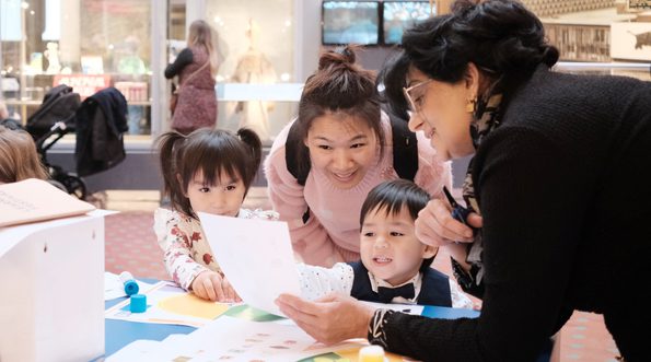 Adults and children looking at paper resource while doing a craft activity.