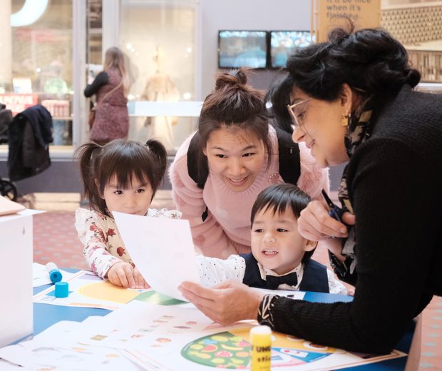 Adults and children looking at paper resource while doing a craft activity.