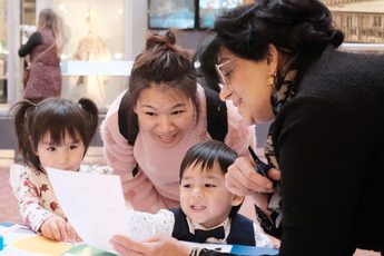 Adults and children looking at paper resource while doing a craft activity.