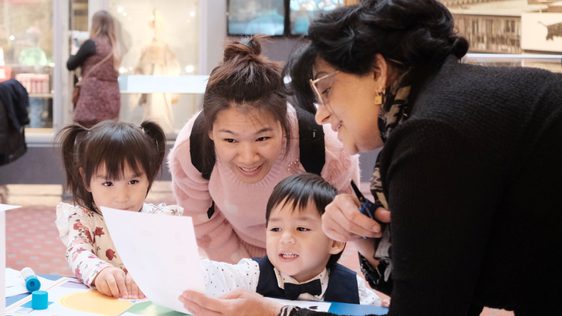 Adults and children looking at paper resource while doing a craft activity.