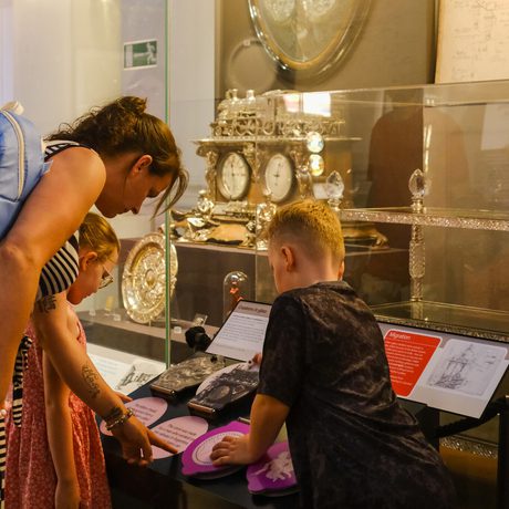 A woman and two children examine historical artefacts in a museum exhibit.