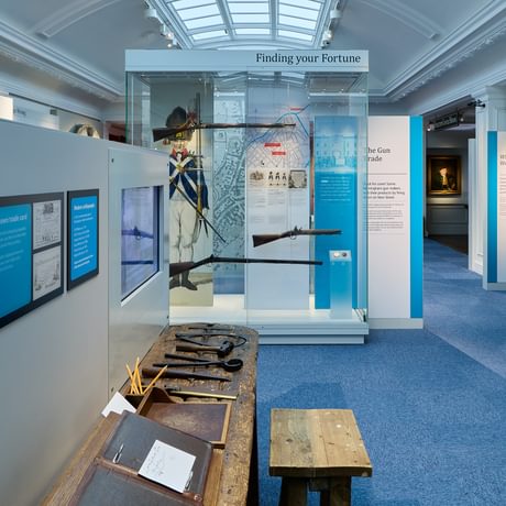 Display with tools on a bench and display case with historic guns.