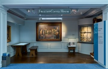 A relicapa style historic coffee house with painting on display and sign that reads ' Freeth's Coffee House'.