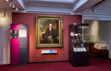 A painting in a gold frame on display alongside a display case.
