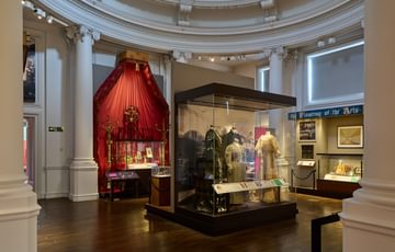 A circular room with display cases some of which contain historic dresses and costumes.