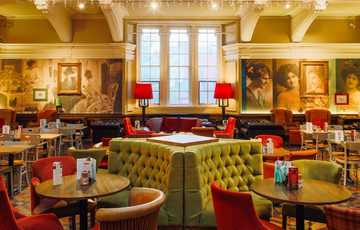 Elegant, spacious restaurant with vintage decor, tufted seating, warm lighting, and large wall portraits.