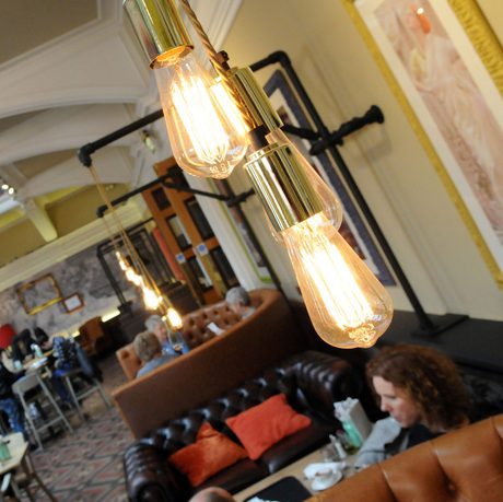 Vintage Edison bulbs illuminate a cozy, bustling tearoom with casual seating and relaxed people.