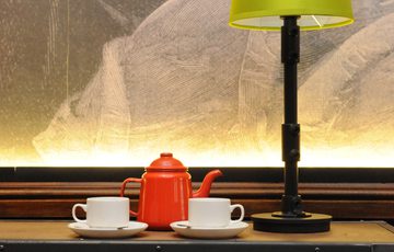 A cozy setup with two teacups, a red teapot, and a green lampshade on a table.