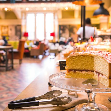 Victoria sponge cake on a stand there is a busy café in the background