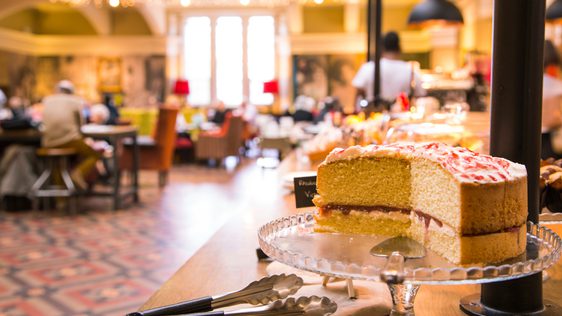 Victoria sponge cake on a stand there is a busy café in the background