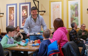 A family sitting in a tearoom with a person delivering a tray of food.