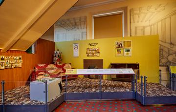 A display called 'Making Home' featuring a recreate lounge with sofa, fireplace, radiogram and photos on the walls.