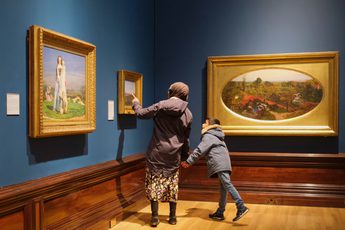 An adult and child looking at paintings in gold frames on display in an art gallery.
