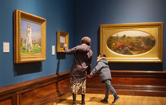 An adult and child looking at paintings in gold frames on display in an art gallery.