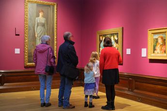 A family with adults and children looking at paintings on display in an art gallery.