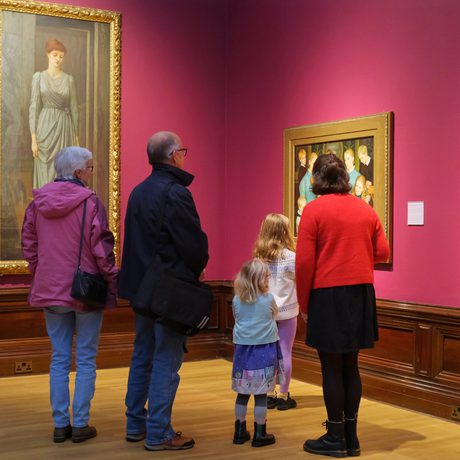 A family with adults and children looking at paintings on display in an art gallery.