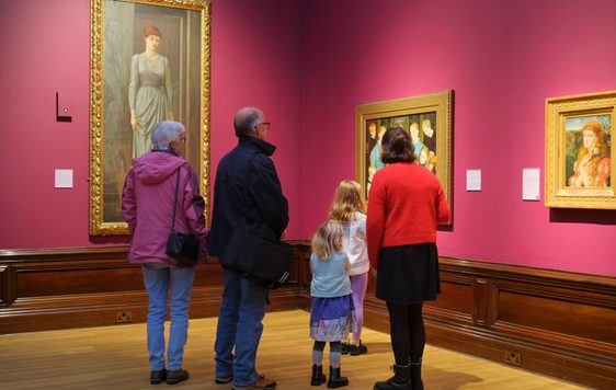 A family with adults and children looking at paintings on display in an art gallery.