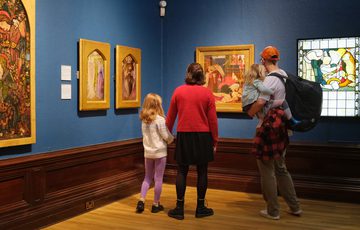 A family looking at paintings in gold frames and stained glass on display in an art gallery.