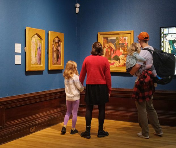 A family looking at paintings in gold frames and stained glass on display in an art gallery.