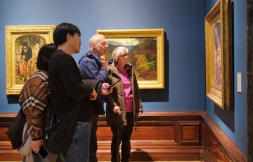 A group of people looking a painting in a gold frame on display in a gallery.