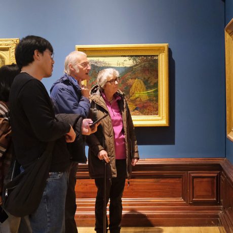 A group of people looking a painting in a gold frame on display in a gallery.