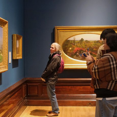 A group of people looking at paintings in gold frames on display in an art gallery.