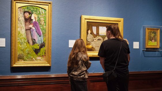An adult and child looking at paintings in gold frames on display in an art gallery.