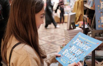A child holding a book 'People Need People' by Benjamin Zephaniah which is for sale in the shop.