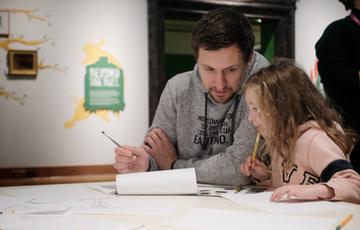 An adult and child sitting at a desk and drawing.