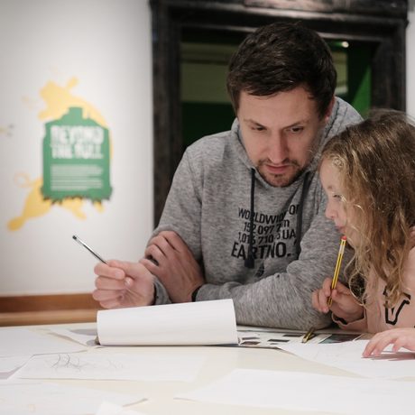 An adult and child sitting at a desk and drawing.
