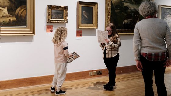 Two children and adults looking at paintings on display.