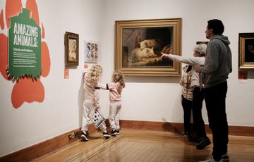 Two children and adults looking at paintings on display.