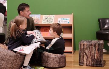 An adult and two children sitting reading booking in reading area.