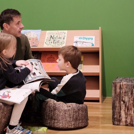 An adult and two children sitting reading booking in reading area.