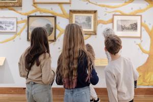Back of heads of three children looking at paintings on display.