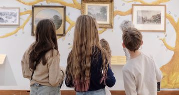 Back of heads of three children looking at paintings on display.