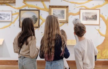 Back of heads of three children looking at paintings on display.