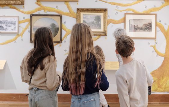 Back of heads of three children looking at paintings on display.