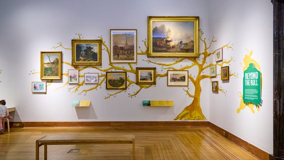 A gallery wall with paintings on display and a tree painted on the wall.