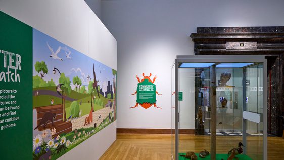 A gallery display with graphic on wall and display case with taxidermy animals.