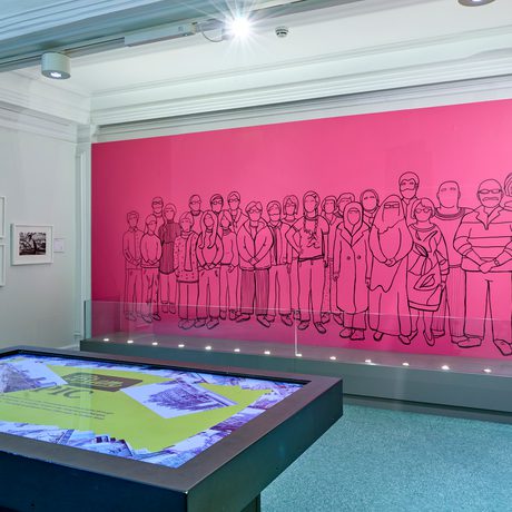 Outline mural of Citizen's Jury participants on a pink wall in front of a touch table and photographs on the wall.