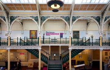 Ornate metal balcony and stairs with two large paintings and a sign with 'Deviance & Difference'