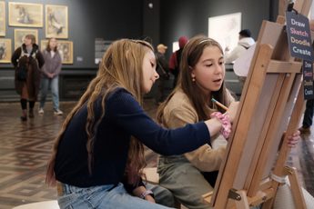 Close up of two children sitting and drawing at an easel in a gallery.