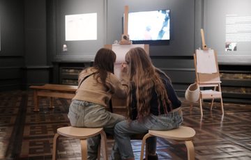 Two children sitting and drawing at an easel.